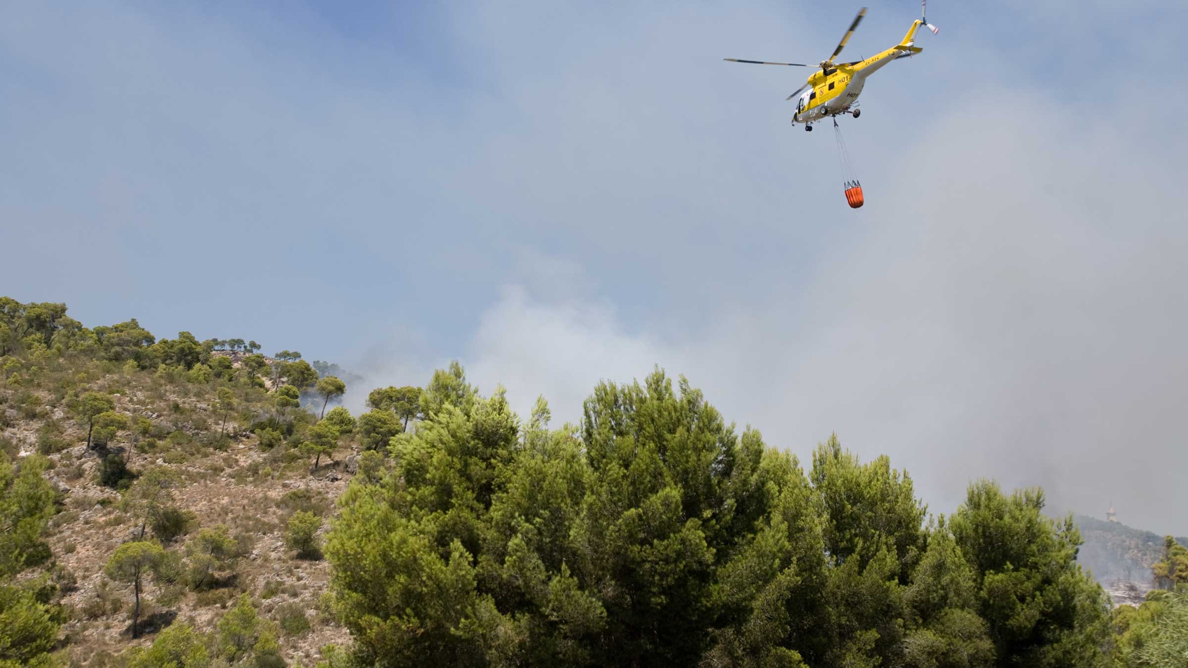 A helicopter dousing flames over a forest fire in Spain
