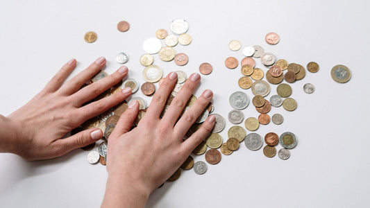 Two hands mixing a variety of coins on a white surface