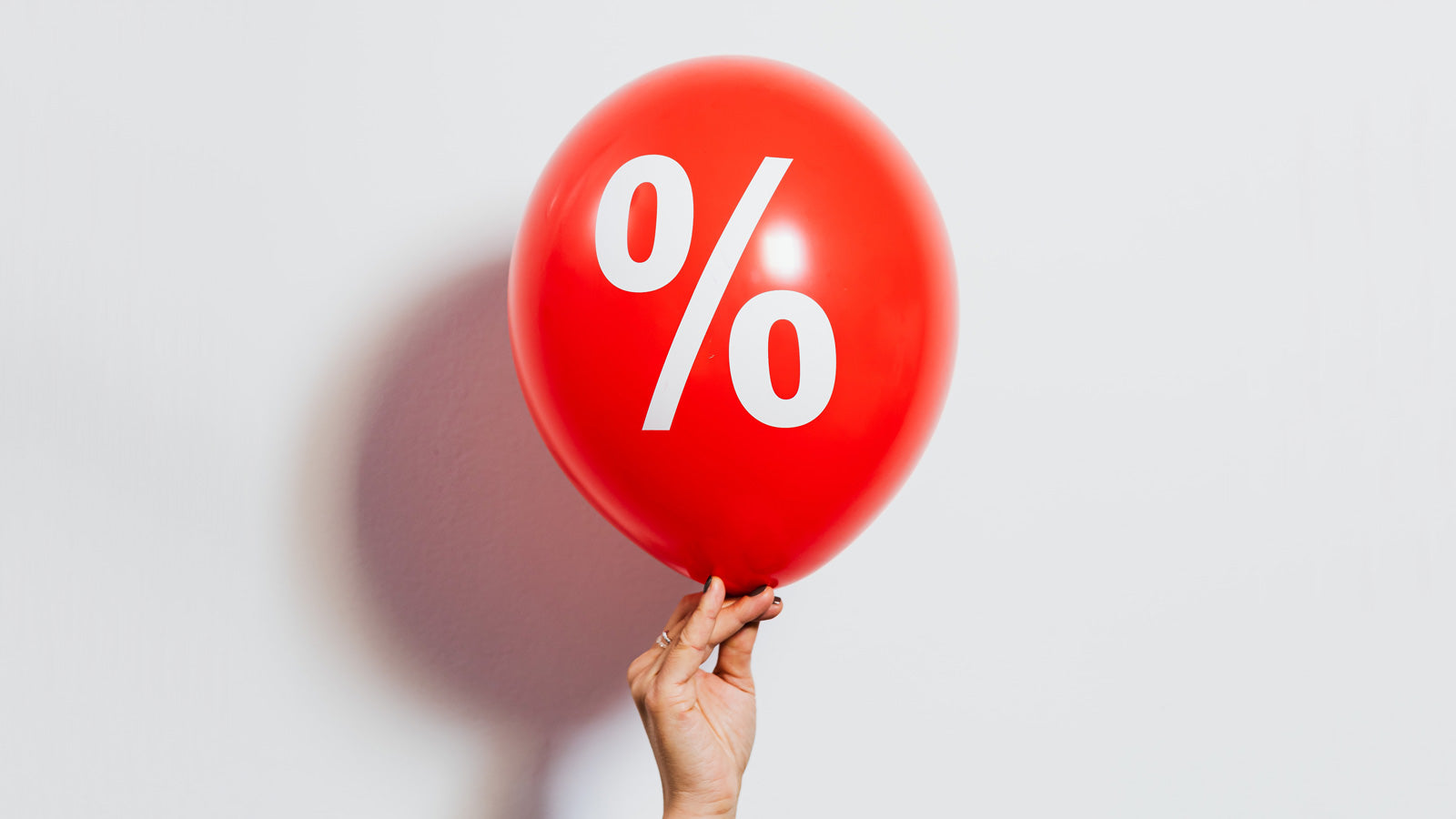 a red balloon with a percent sign printed on it held up against a white background